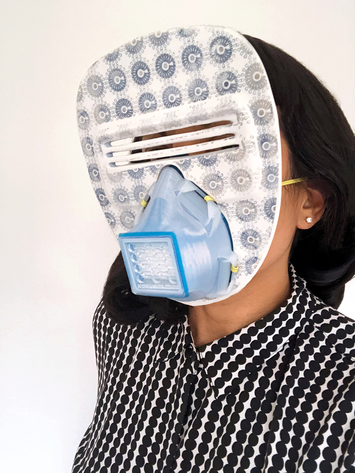 woman in black and white patterned blouse holding an face mask thats part decorative and part protective