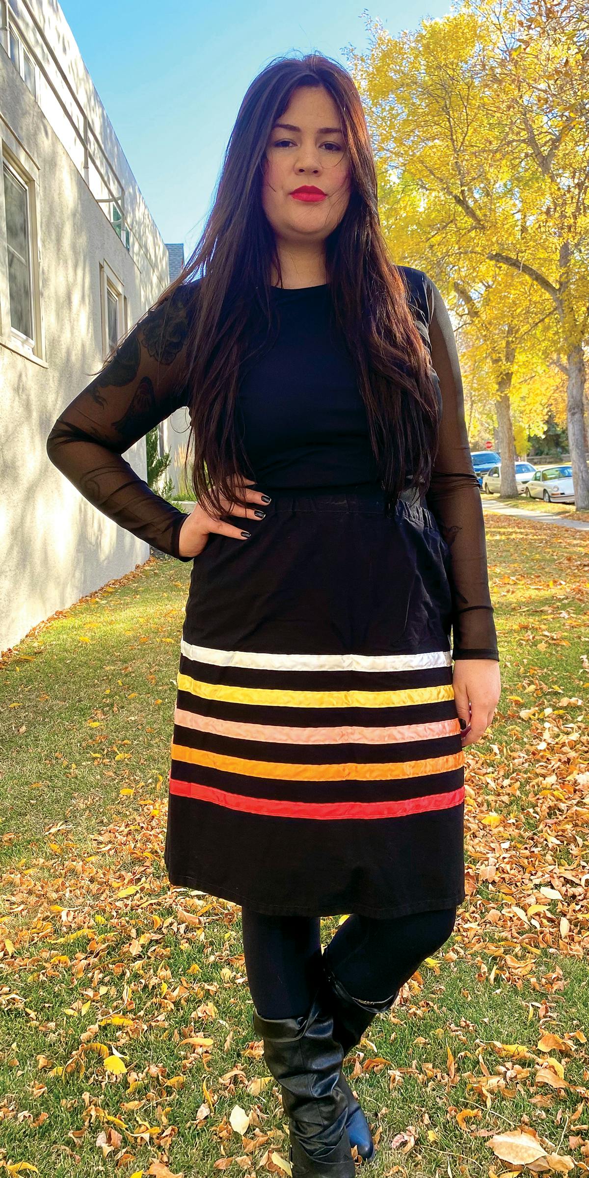 woman standing outside beside a building wearing traditional ribbon skirt