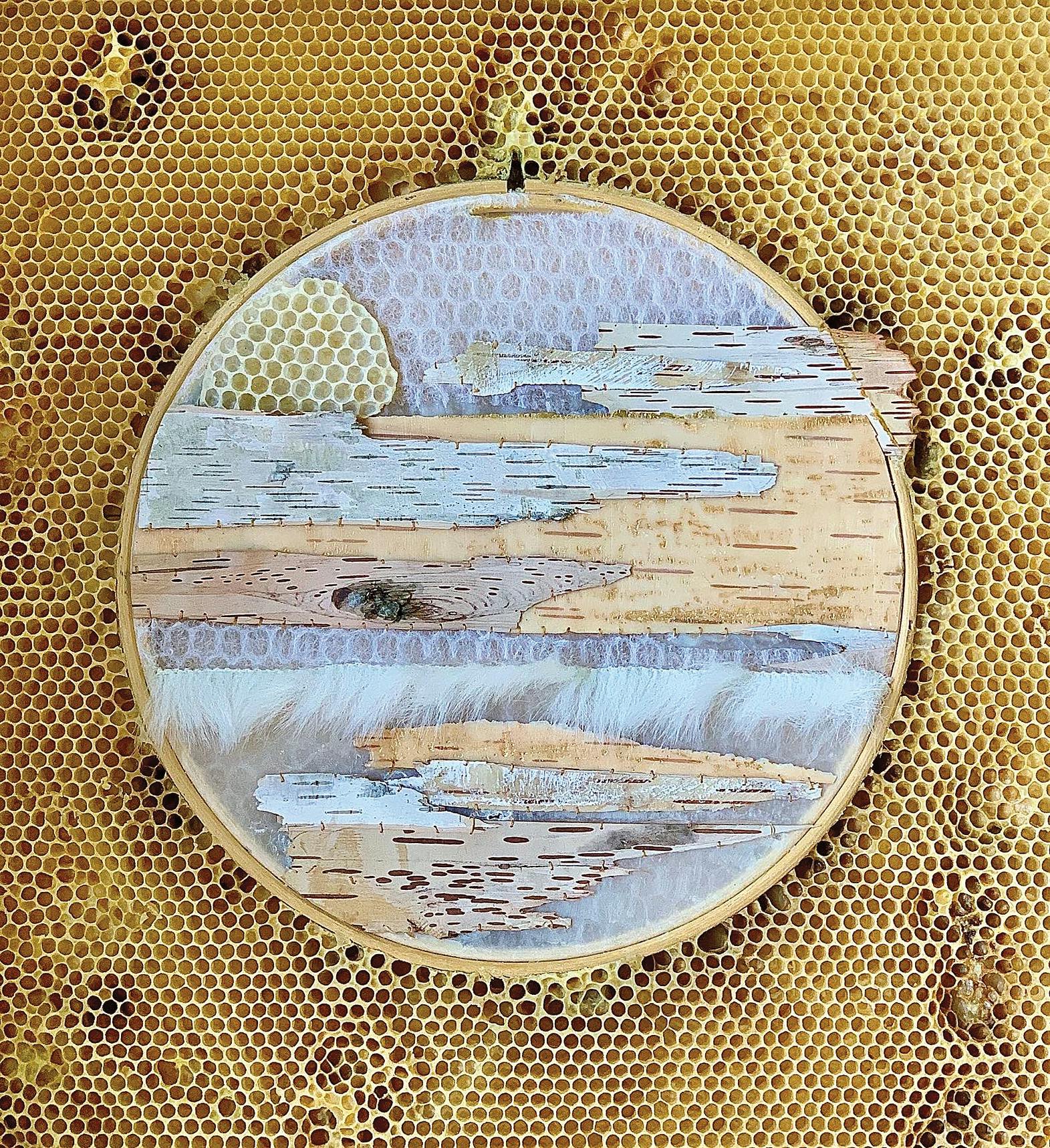 Embroidery hoop with blue fiber and beads embedded in honeycomb with bees