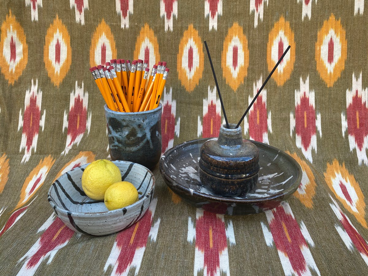 handmade ceramic vessels of different shapes holding lemons incense and pencils arranged against a patterned textile backdrop