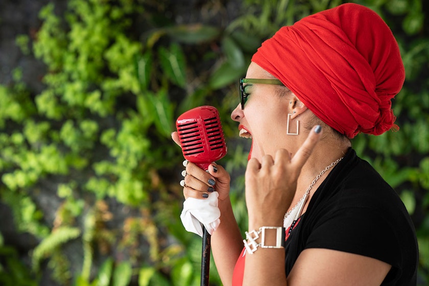 Singer with red headwrap singing into a red microphone