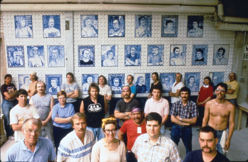 1991 photo of factory workers and an artist posing in front of a wall of ceramic paintings