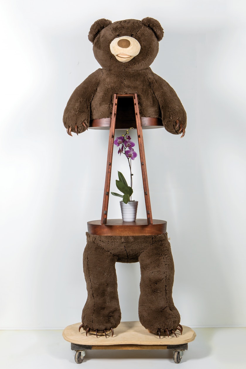 Sculpture of a brown teddy bear with wood claws with a wood cabinet built into its midsection containing a purple orchid
