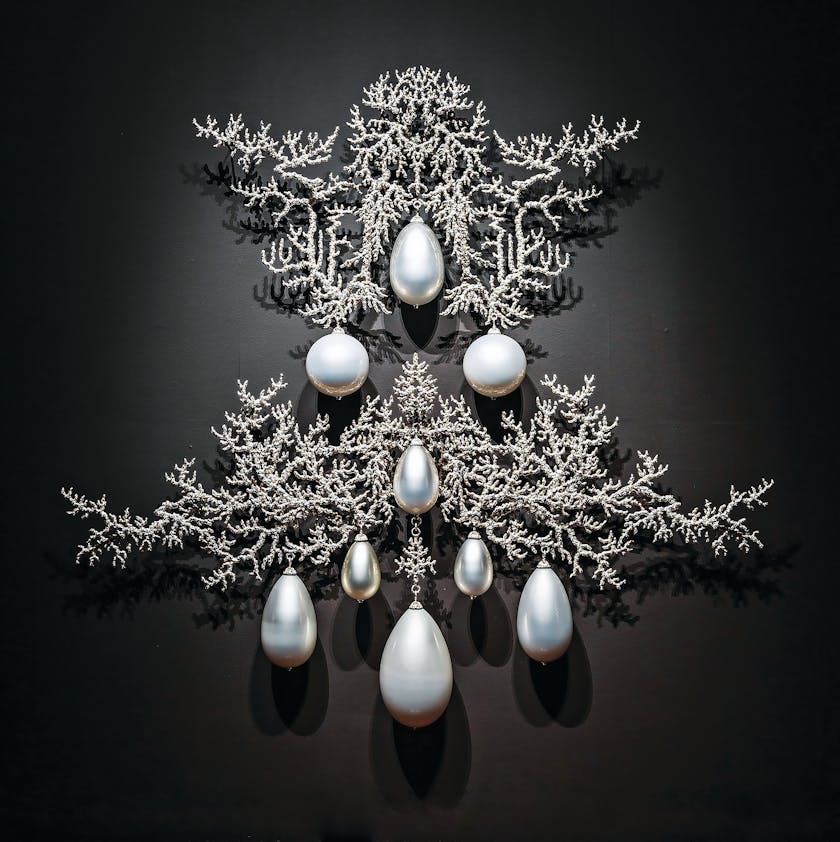 Metallic sculpture on black wall with large hanging pearls amidst fine crusty branches