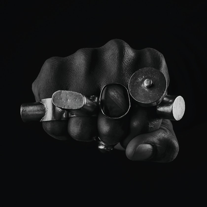 Darkened image of fist adorned with large blocky metallic rings over black background