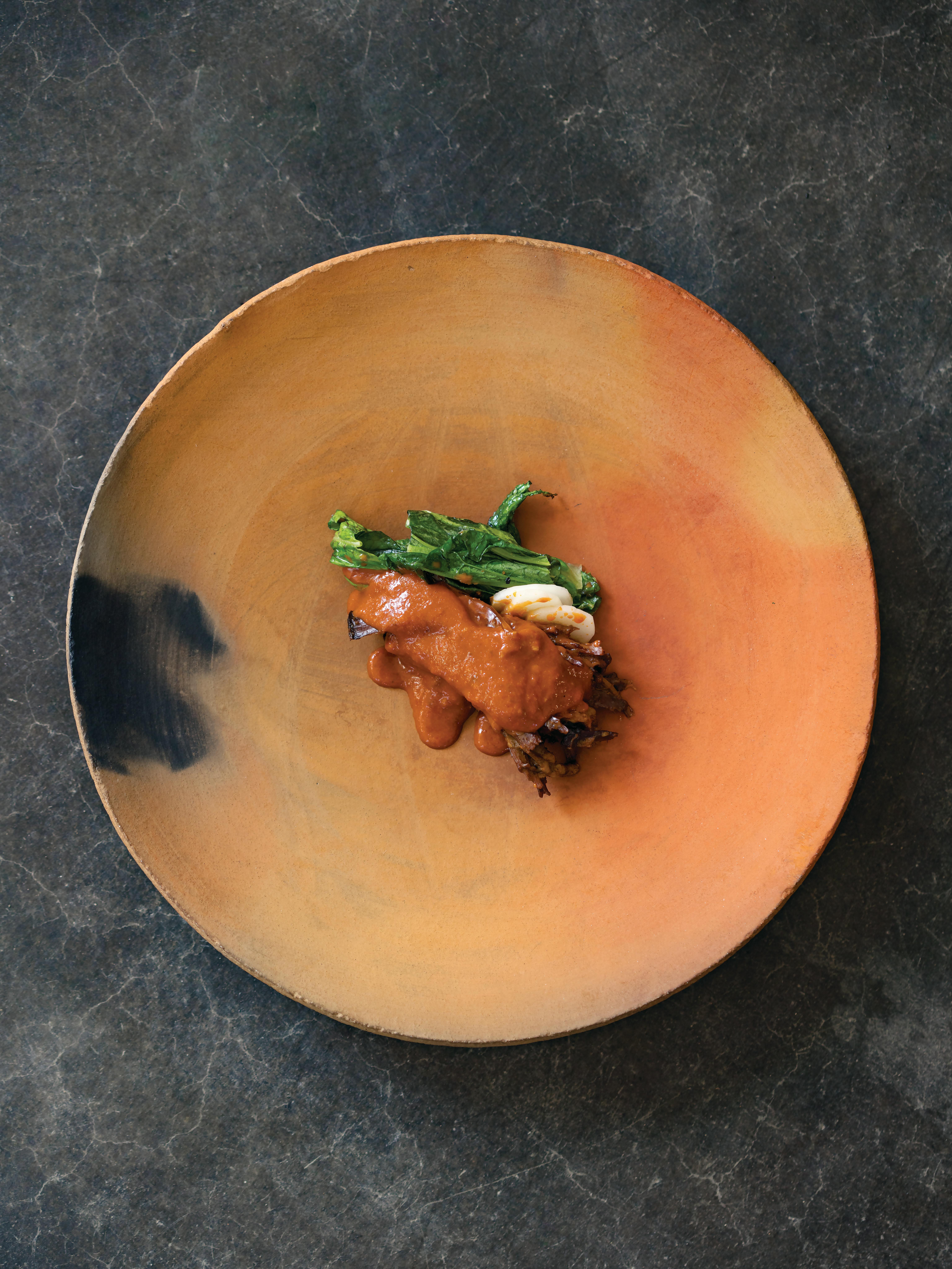 smooth orange plate with smoke smudge with artistically designed saucy beef dish in the center
