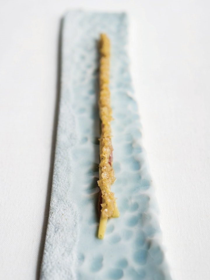 Narrow blue plate textured like a beach with ocean waves holding a long and narrow culinary creation