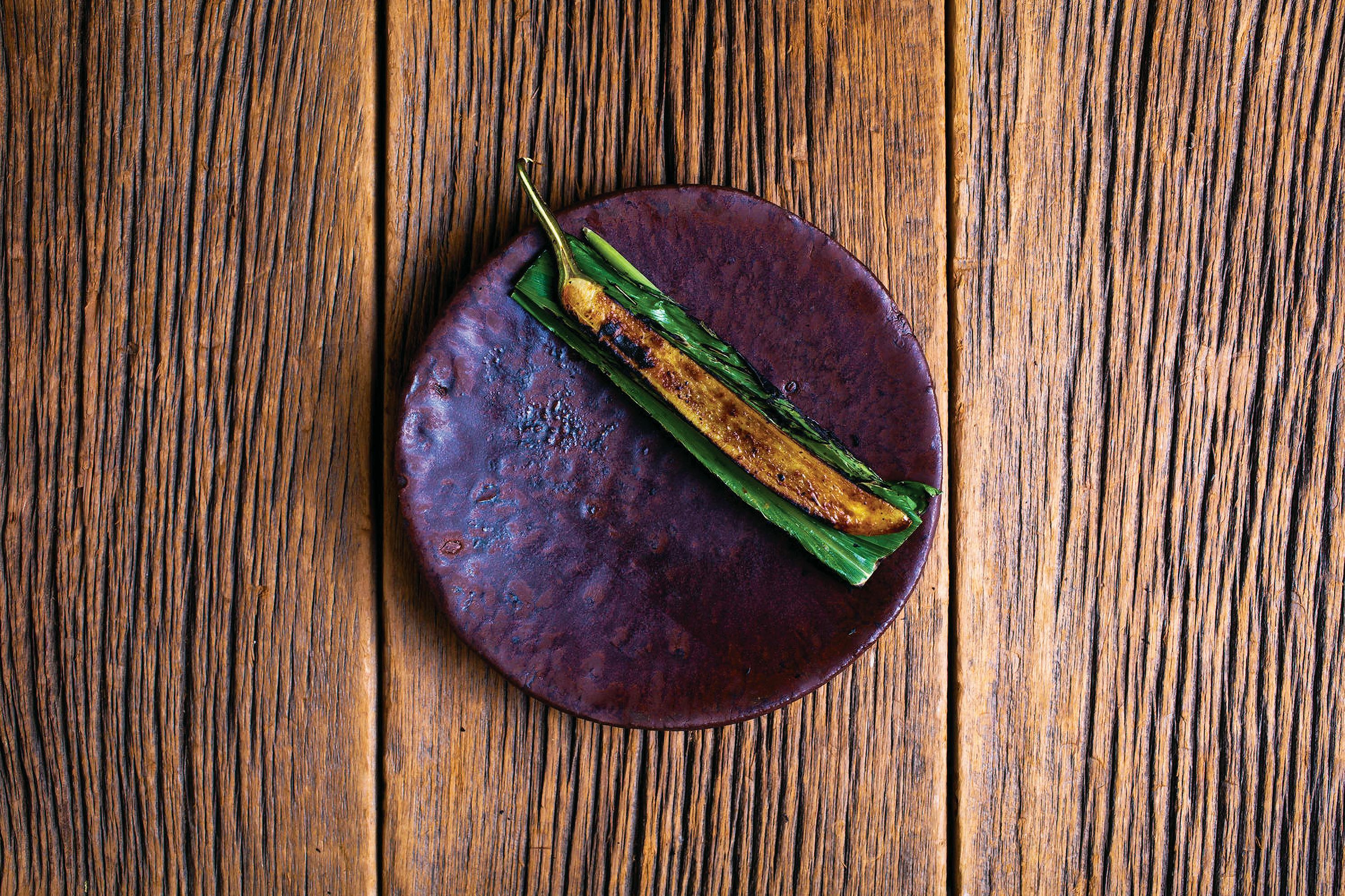 mottled purple ceramic plate with a charred thin eggplant on a folded leaf