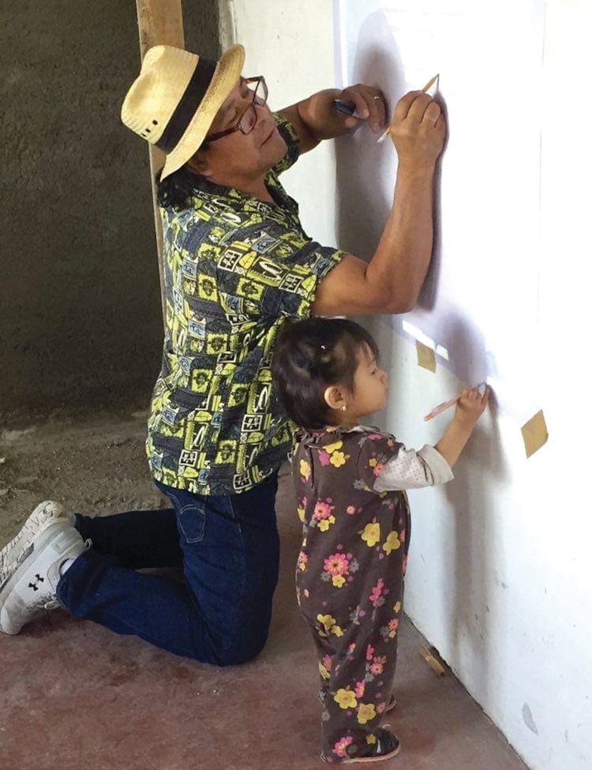 artist working with his daughter on an art project making pencil marks on a wall