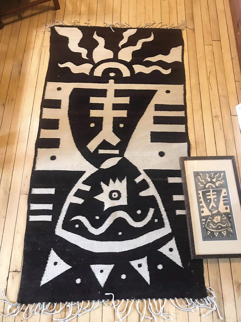 black and white weaving spread out on a wooden floor replicating the design of small painting which is displayed next to the weaving