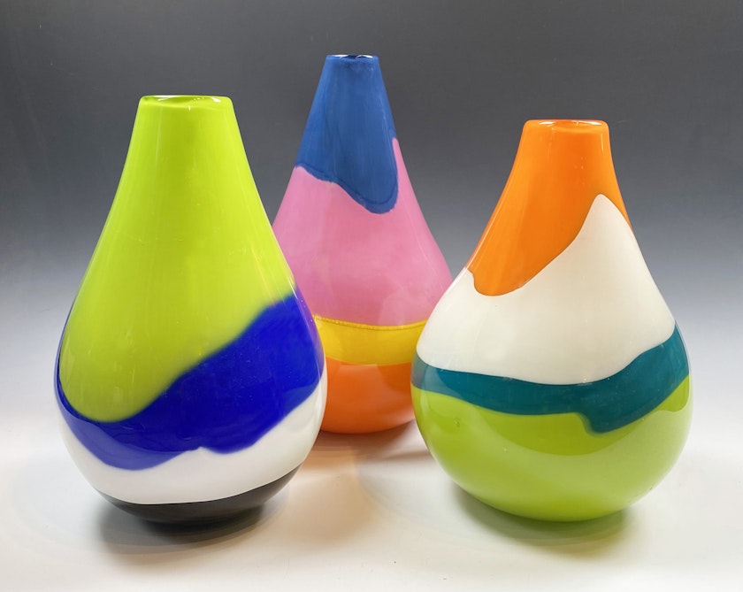 three glass vessels with thick amorphous bands of bright opaque colors. the vessels are pear-shaped with flat tops.