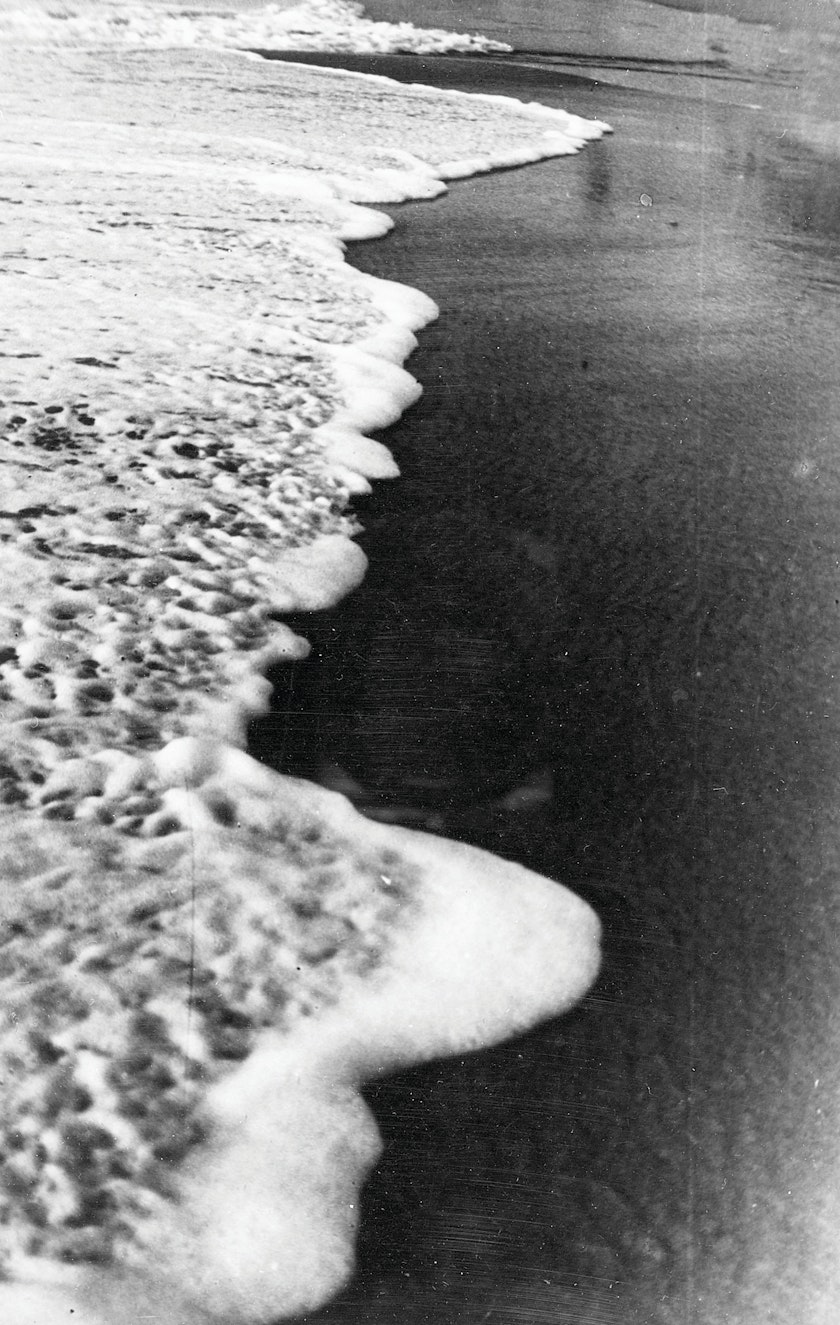 black and white photo of frothy surf washing up on a beach