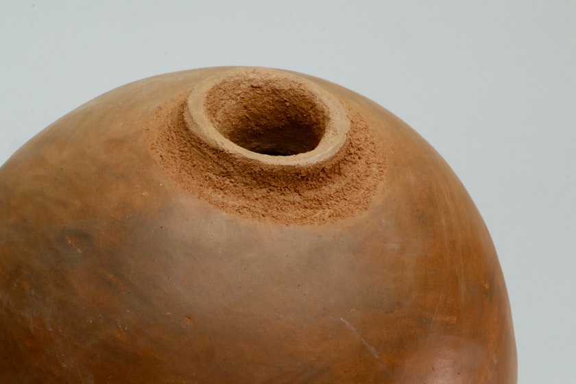 detail of a smooth tan spherical ceramic vessel with a small rough opening