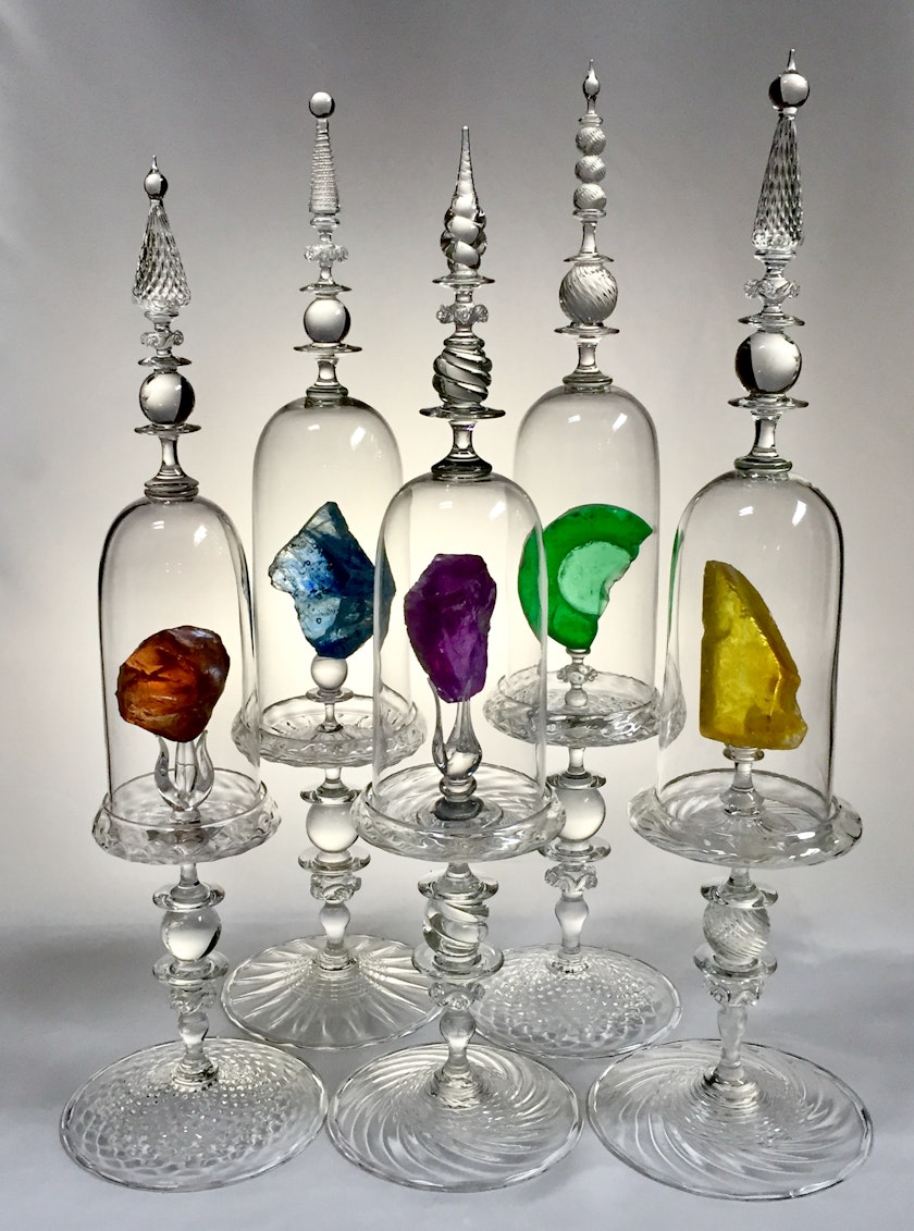 series of ornately sculpted bell jars each containing a glass fragment of a different color