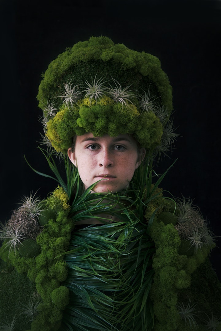 model wearing sculptural hat and suit made from moss grasses and other greenery