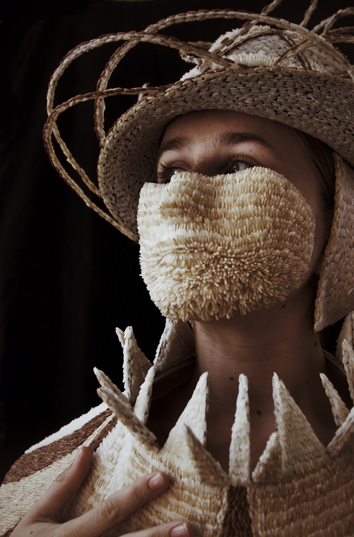 model wearing sculptural hat suit and face mask made from grains of rice