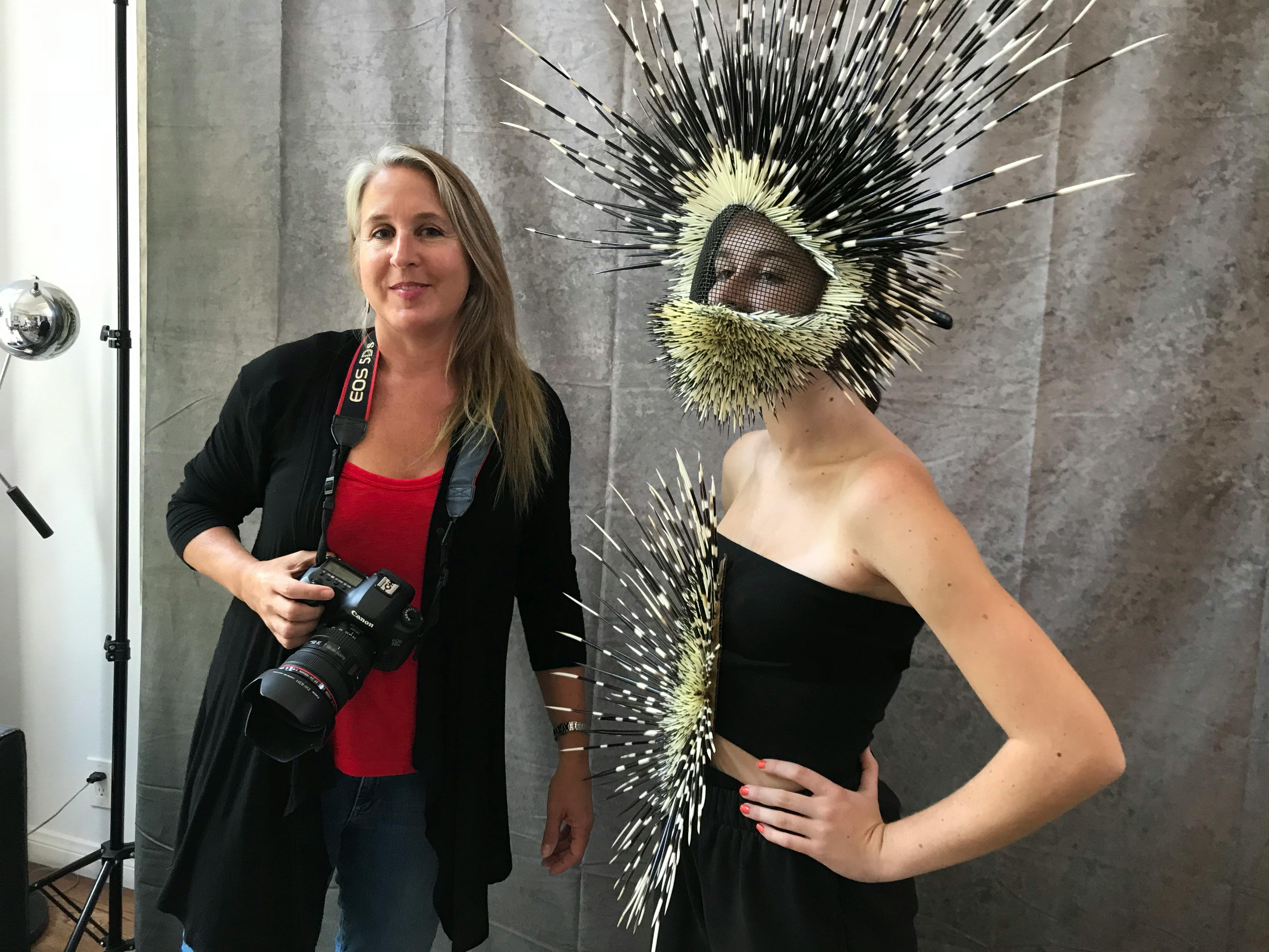 photographer with camera standing beside model wearing a helmet and shirt adorned with porcupine quills