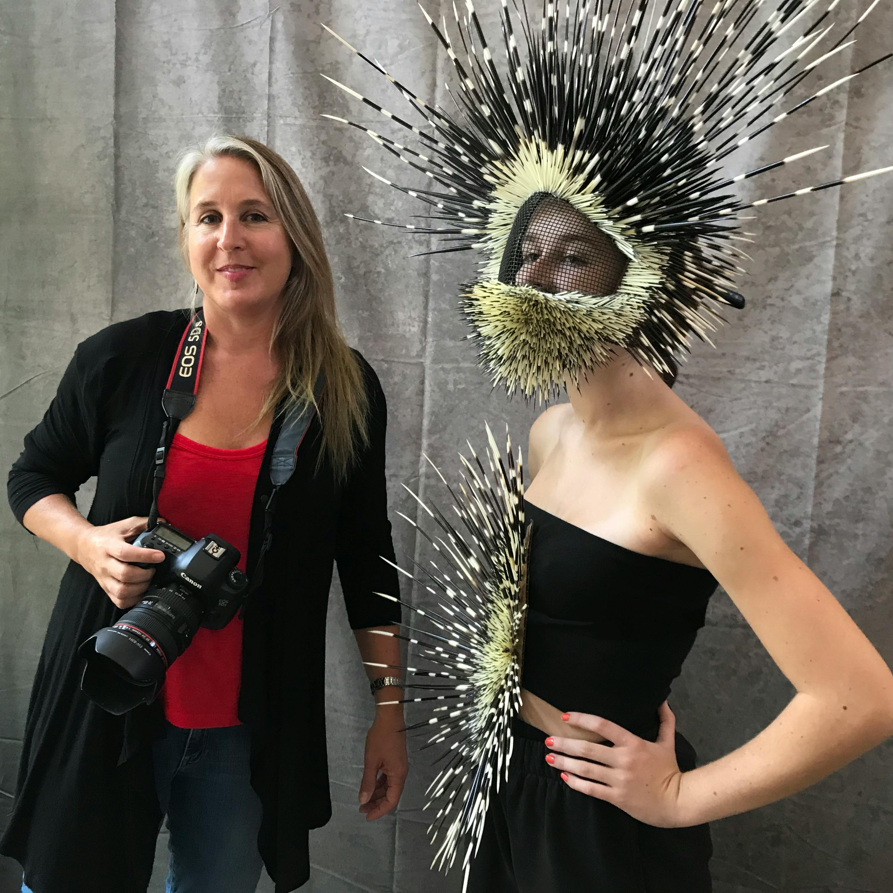 photographer with camera standing beside model wearing a helmet and shirt adorned with porcupine quills