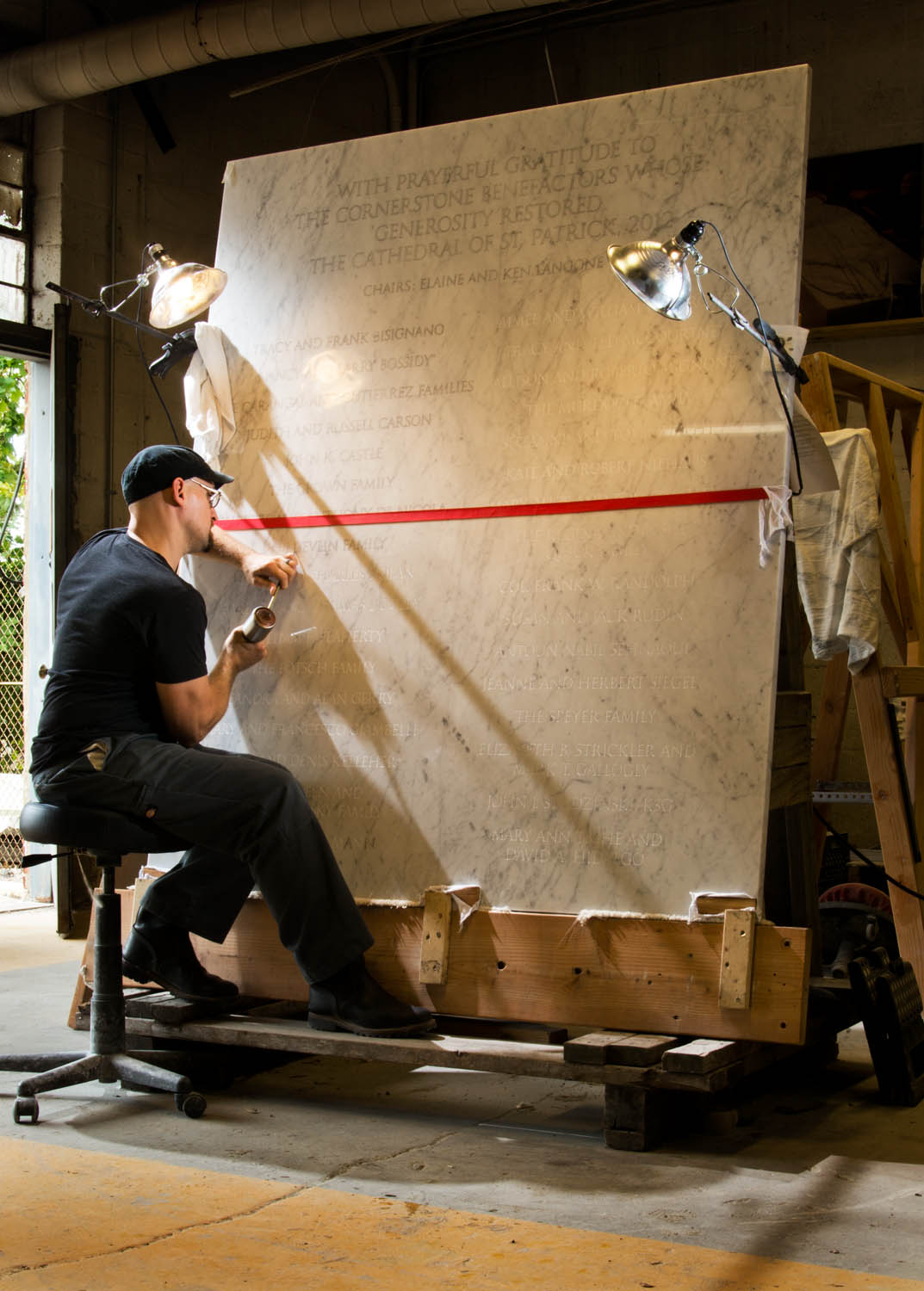 stone carver working on a large marble plaque with names