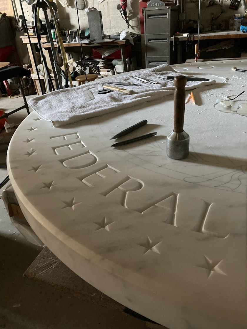 stone carving in progress—a larger round slab with stars and the word federal. Tools are strewn about it.