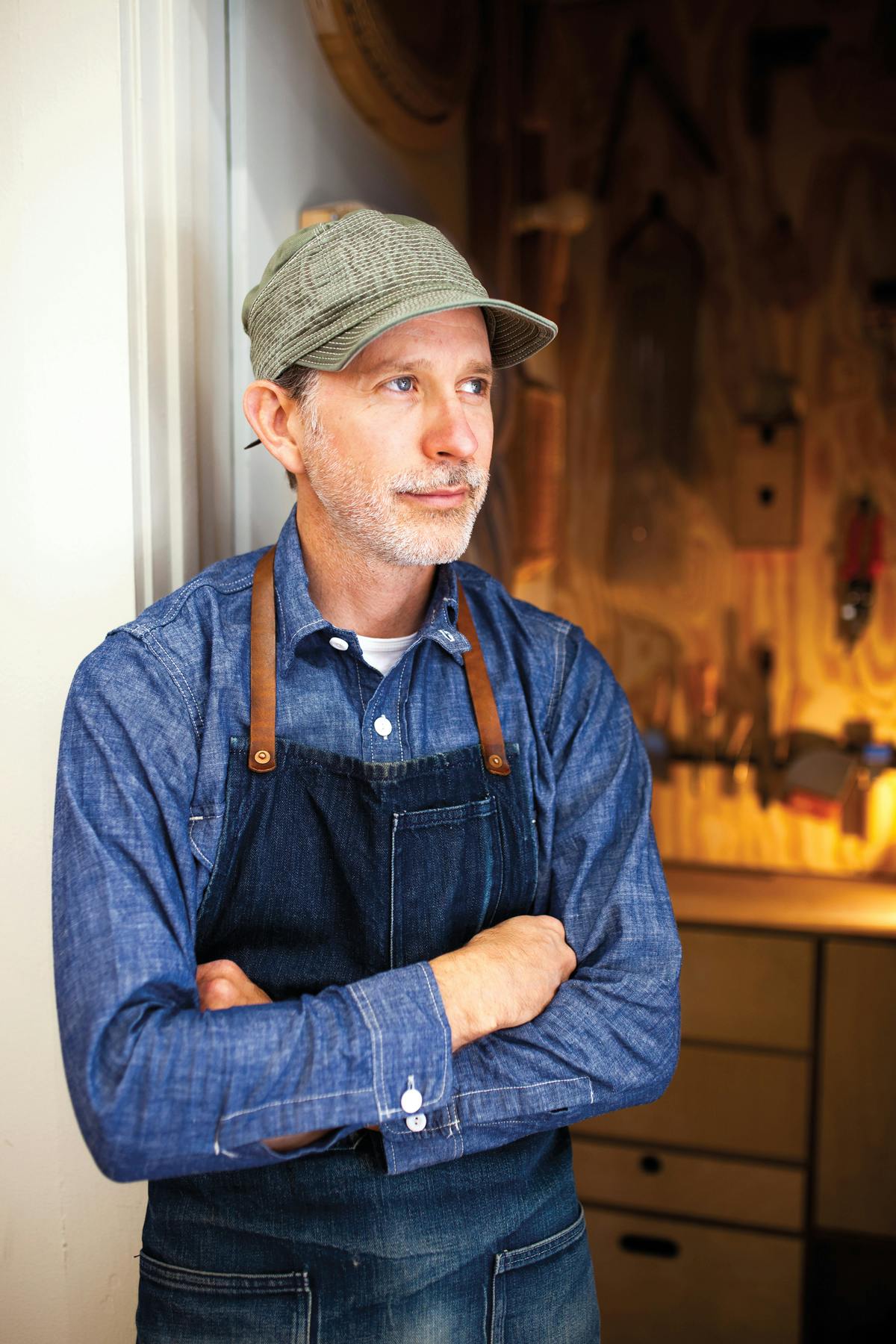 portrait of upholstery artist in studio with arms folded over blue apron