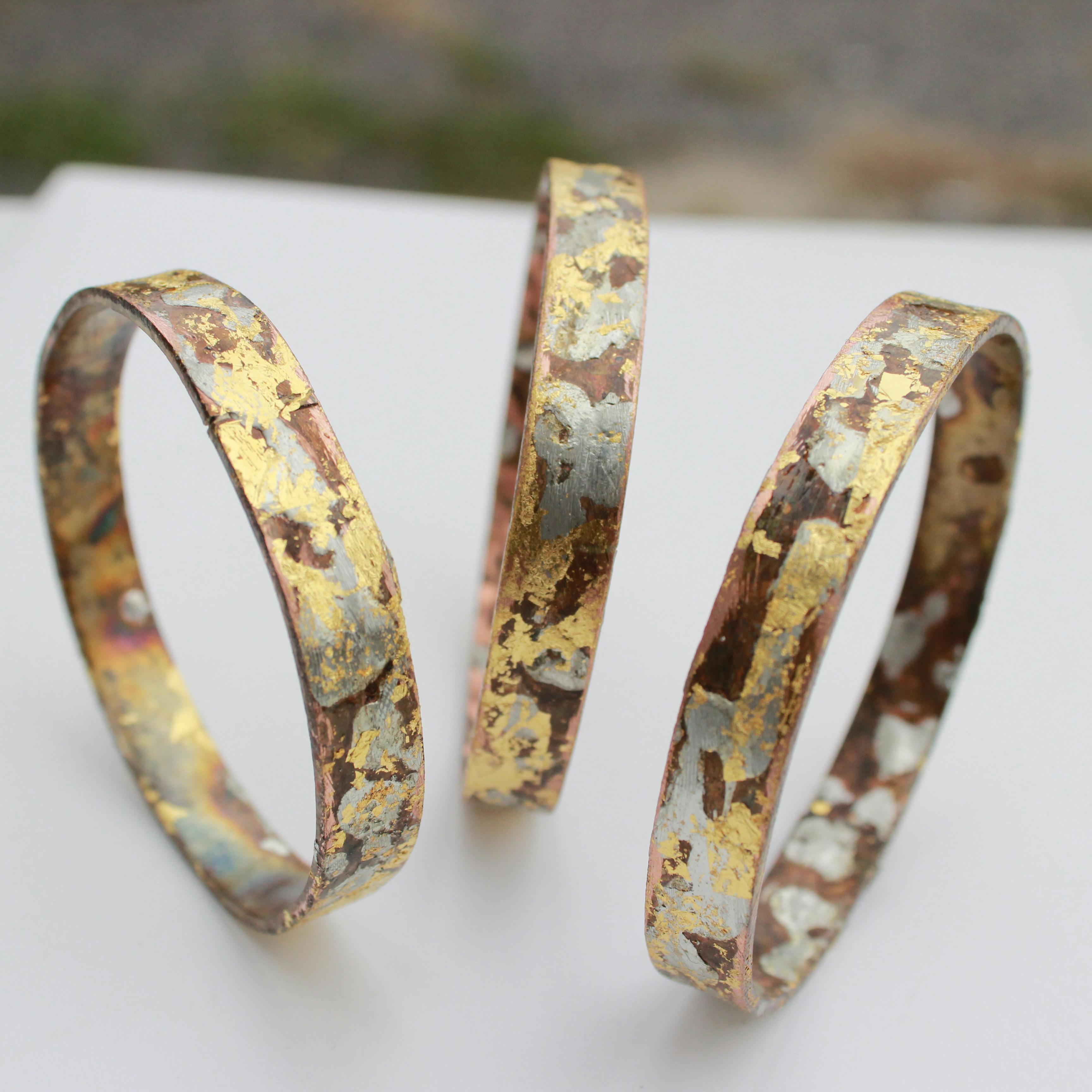 close-up photo of three textured gold and copper bracelets balancing on their sides