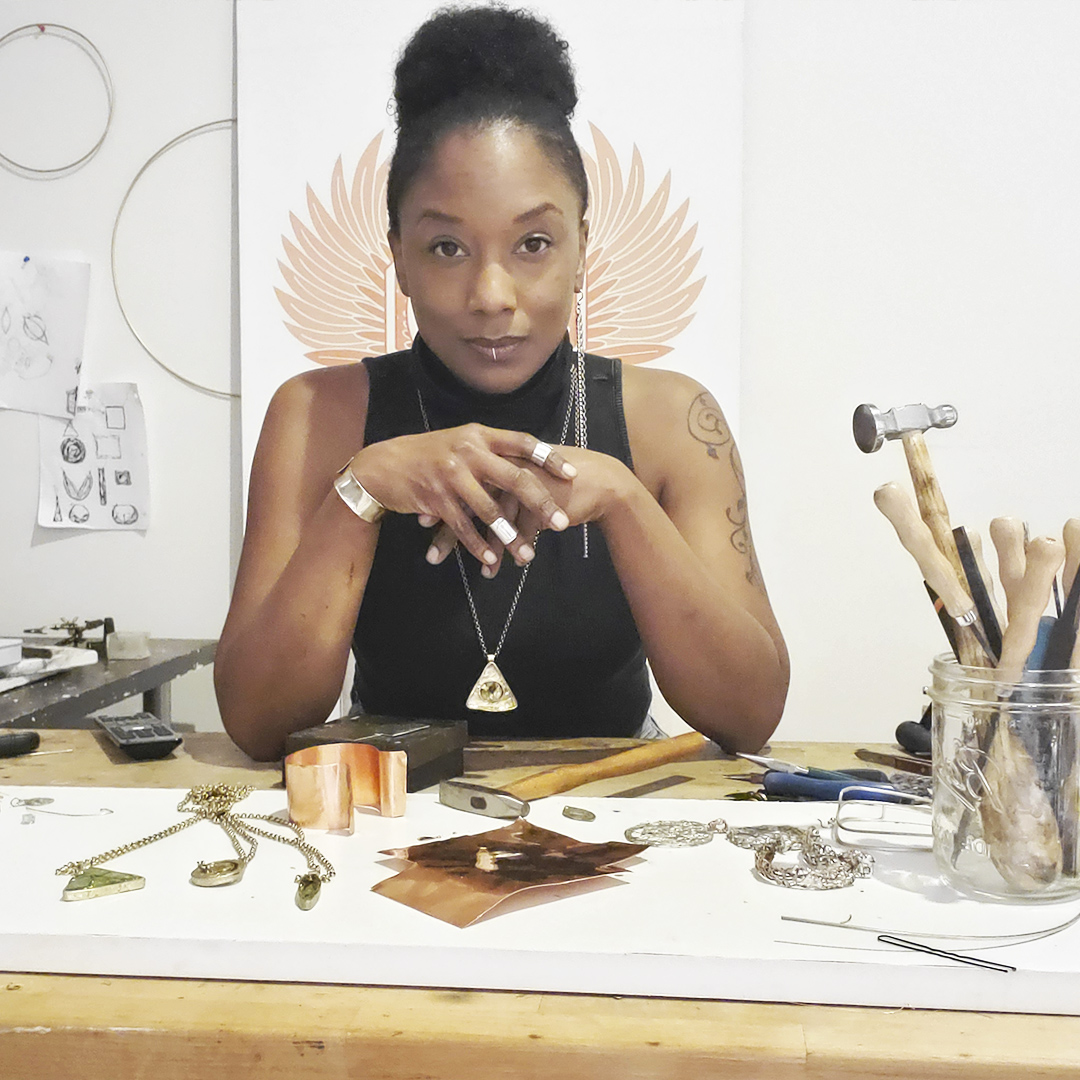 portrait of jewelry artist seated at desk amid tools and works in progress