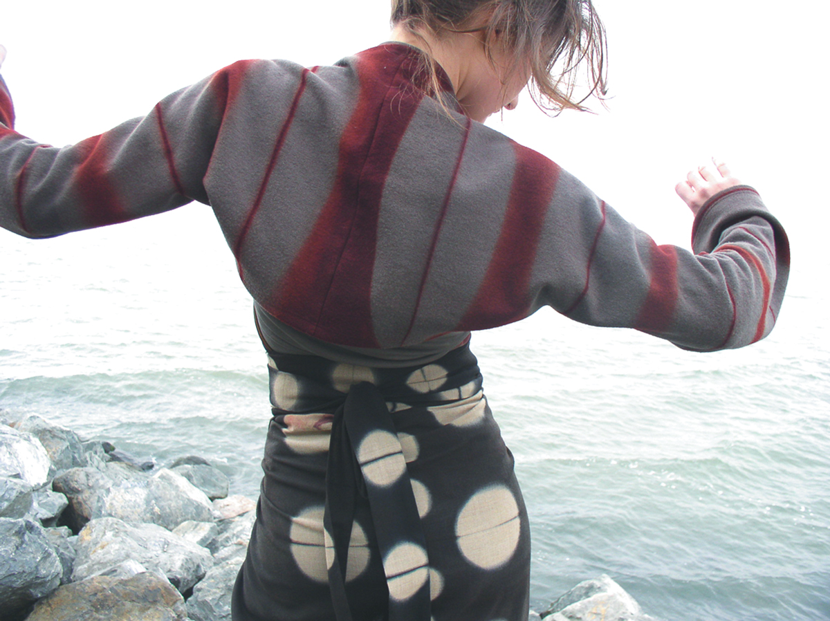 model wearing hand-dyed wool garments facing the sea on a snowy coastline