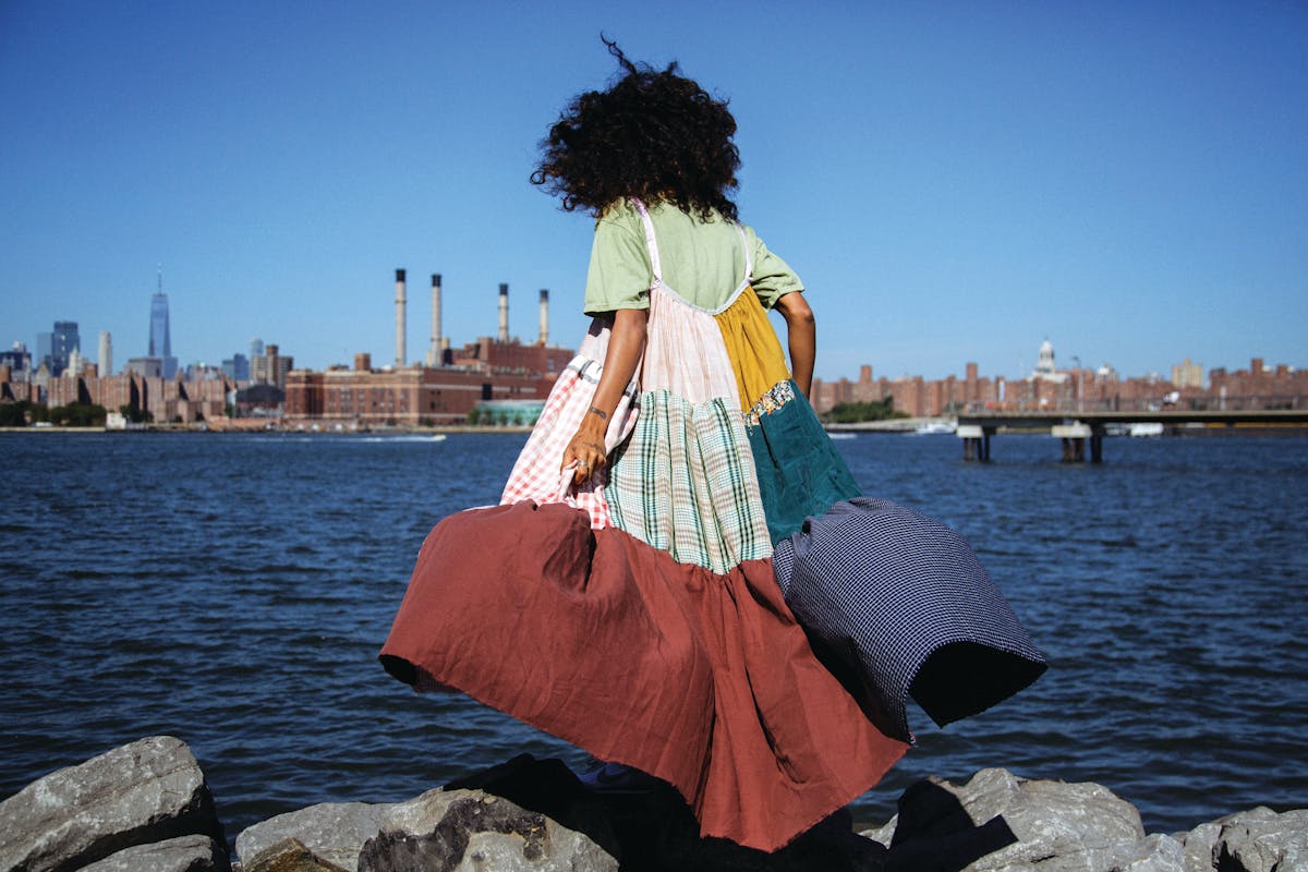 model wearing a patchwork dress on coastline facing water with cityscape in the distance