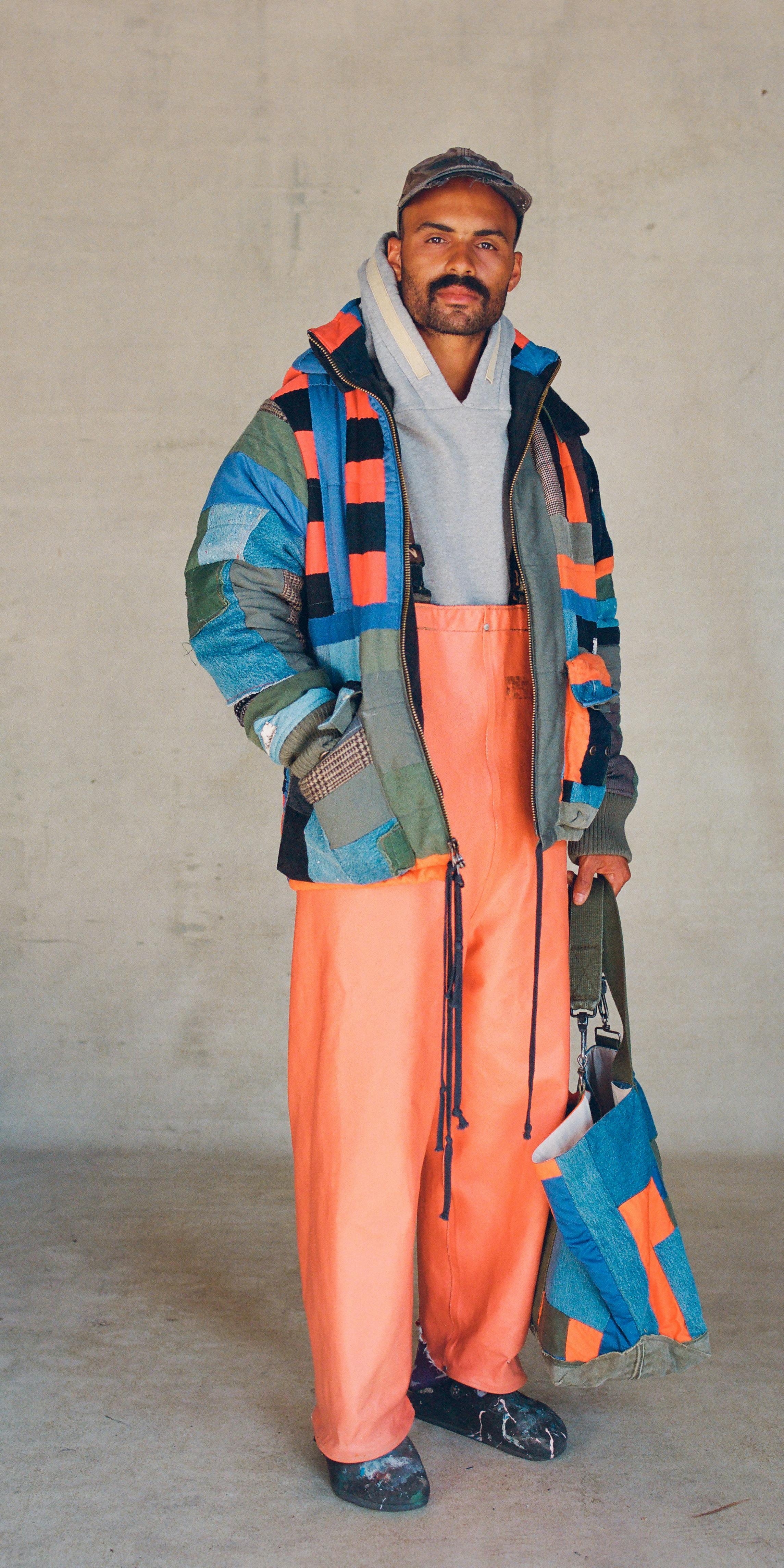 model wearing blue and orange patchwork jacket over orange waders and gray hoodie