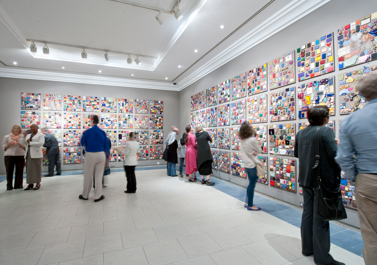 gallery space filled with people viewing wall panels with small handsewn prayer pacakets