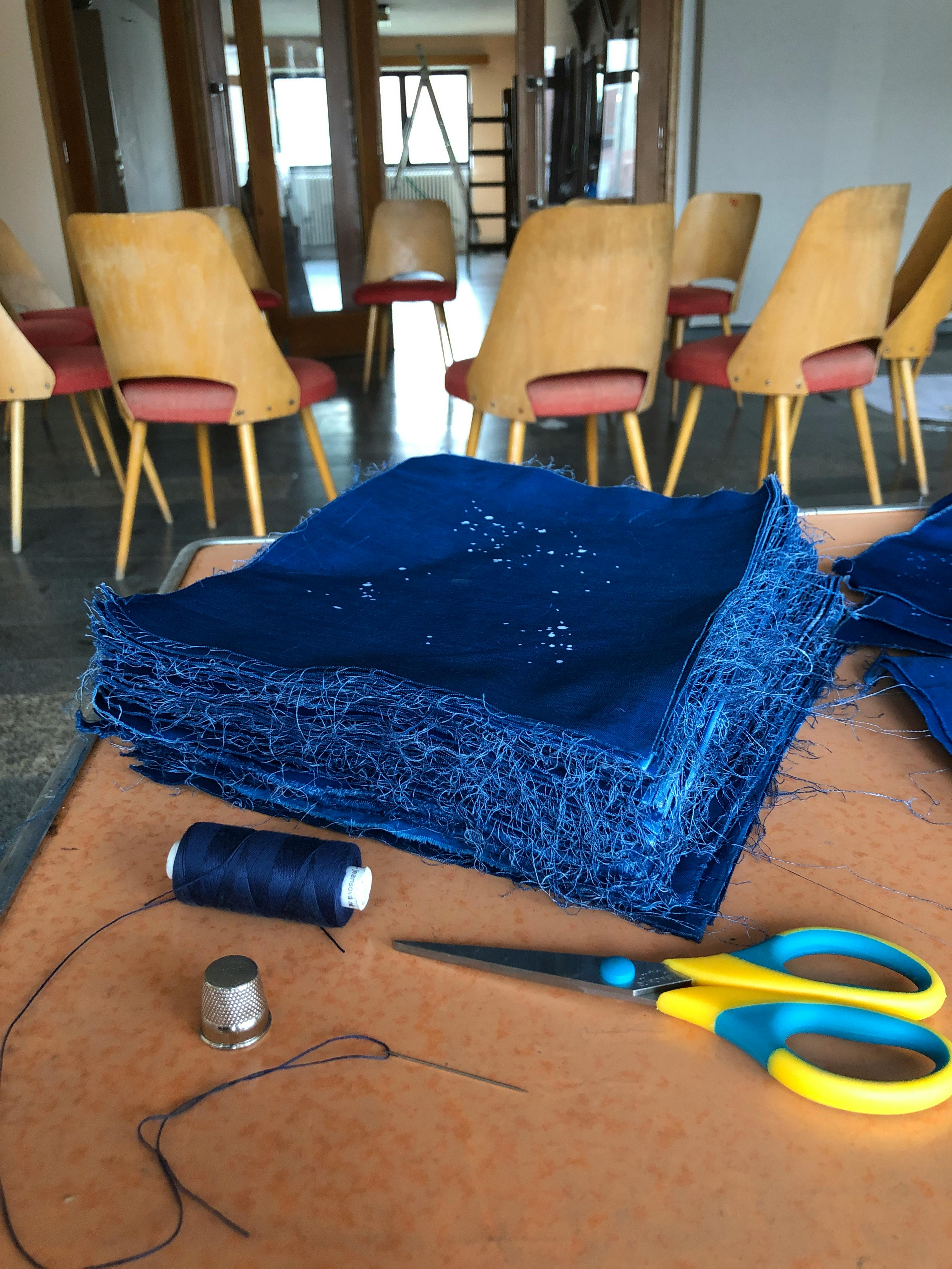 stack of dark blue fabric patches with white specks on a table with sciccors and thread