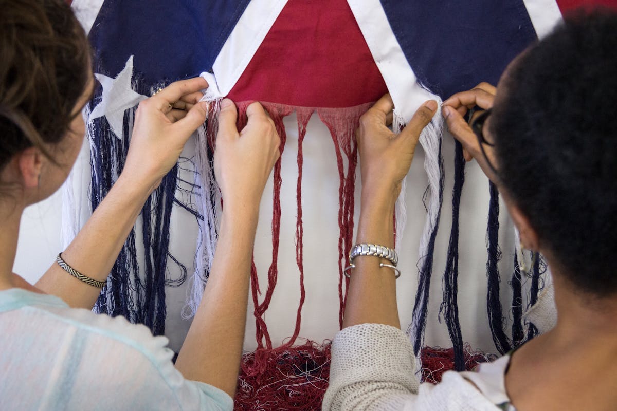 two people using their hands to unravel the fabric of a confederate flag