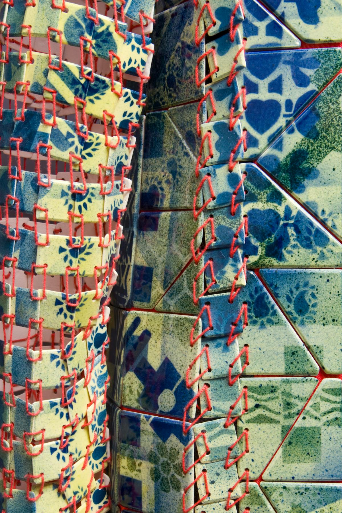 detail of overcoat made from green ceramic tiles sewn together with red thread