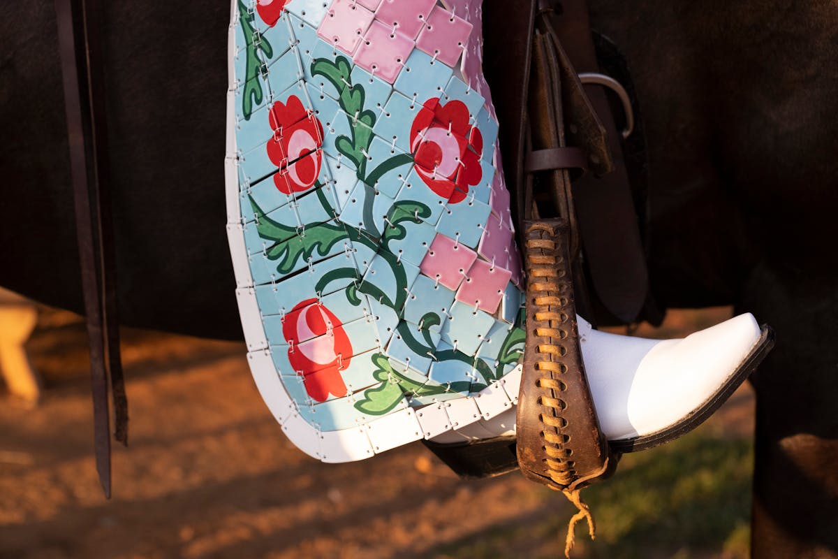 closeup of an leg of ornate pink and blue floral riding chaps made from ceramic tiles with white boot in a stirrup