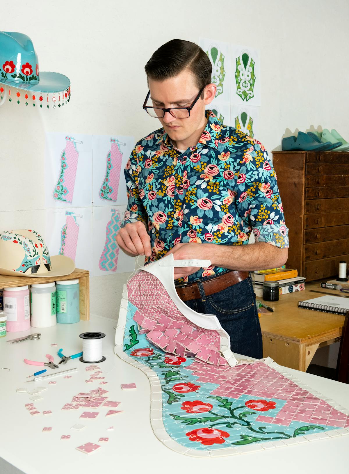 fashion artist sewing a ornate floral pink and blue chaps made from tiles