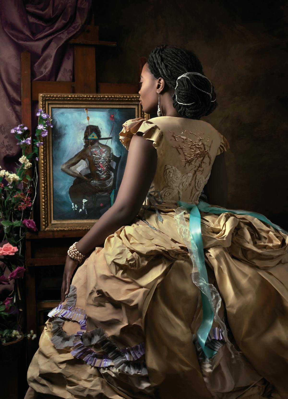 model wearing an ornte gold paper dress standing before a surrealist painting depicting a man seated on a chair