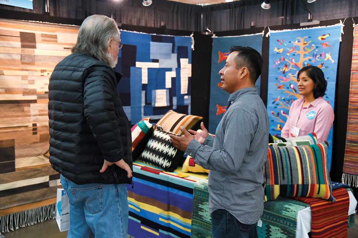 a craft artist at their booth at a craft work displaying their work to shoppers