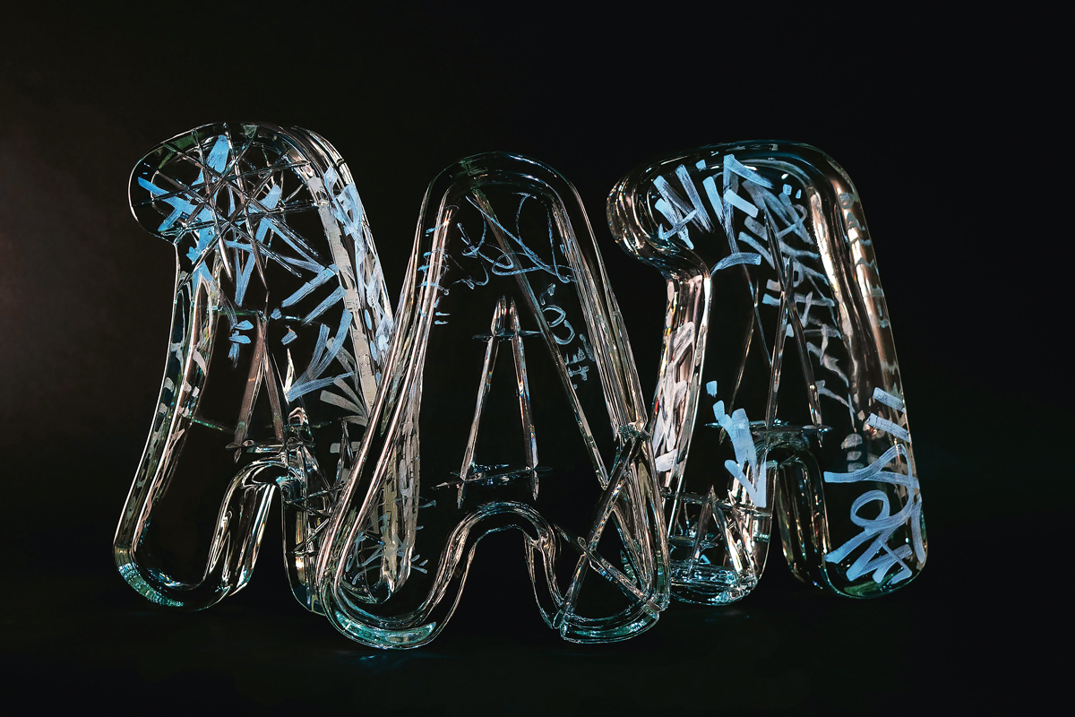 three clear glass sculptures of the letter a with marker writing on them
