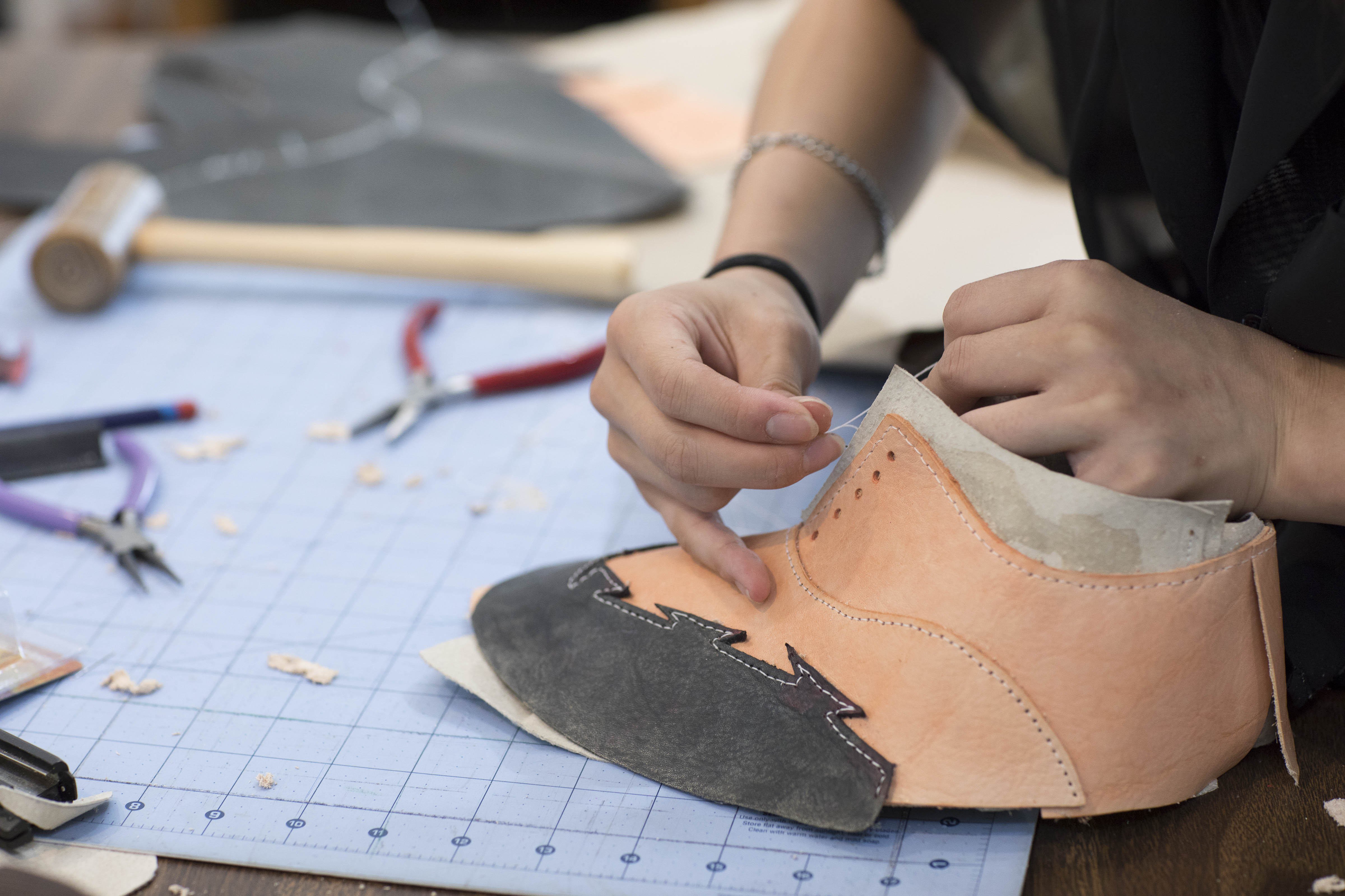 persons hands working on a handmade leather shoe on a shop table