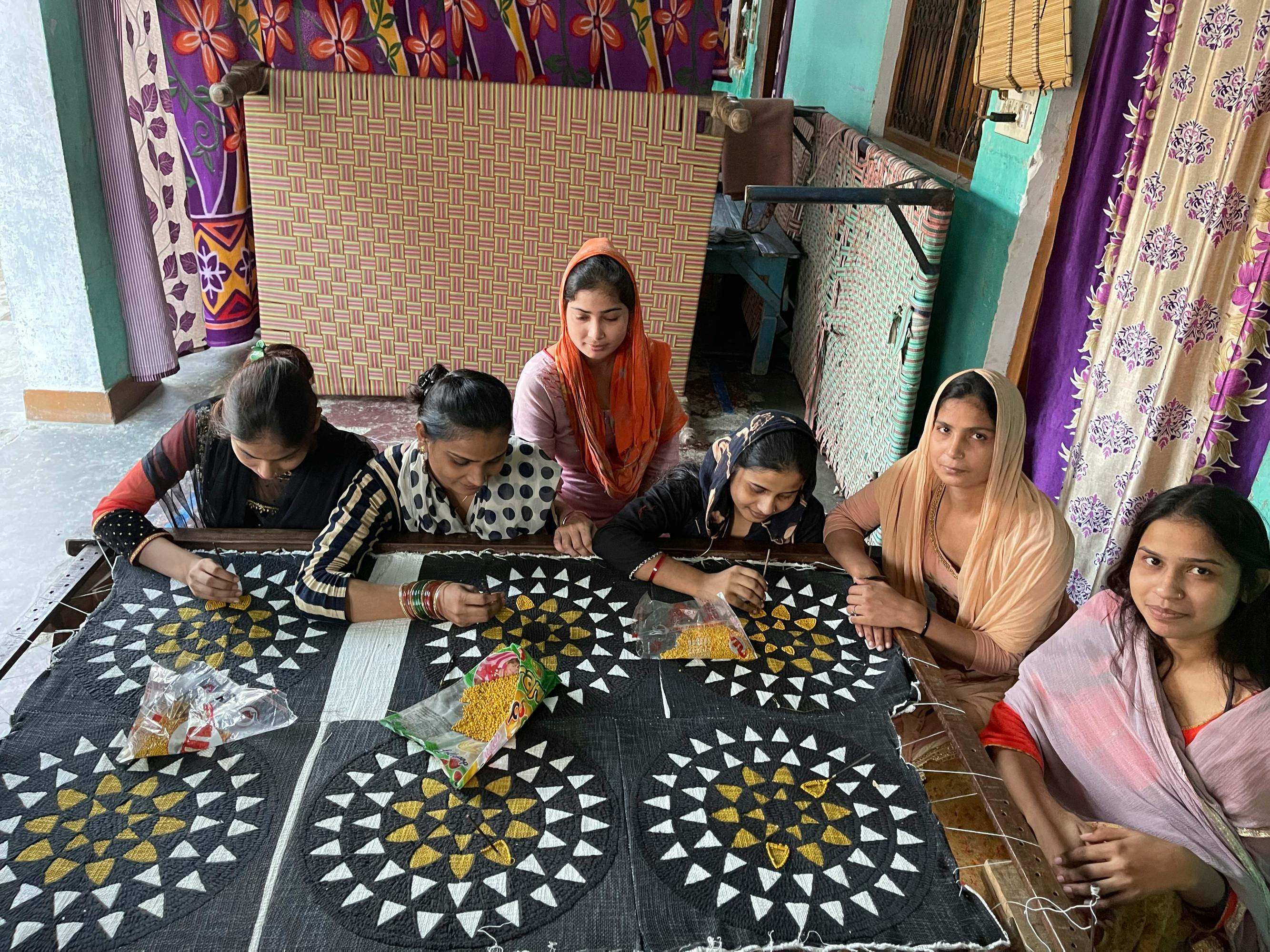 group of artists sitting around a table in india working on a series of black white and yellow patterned textiles