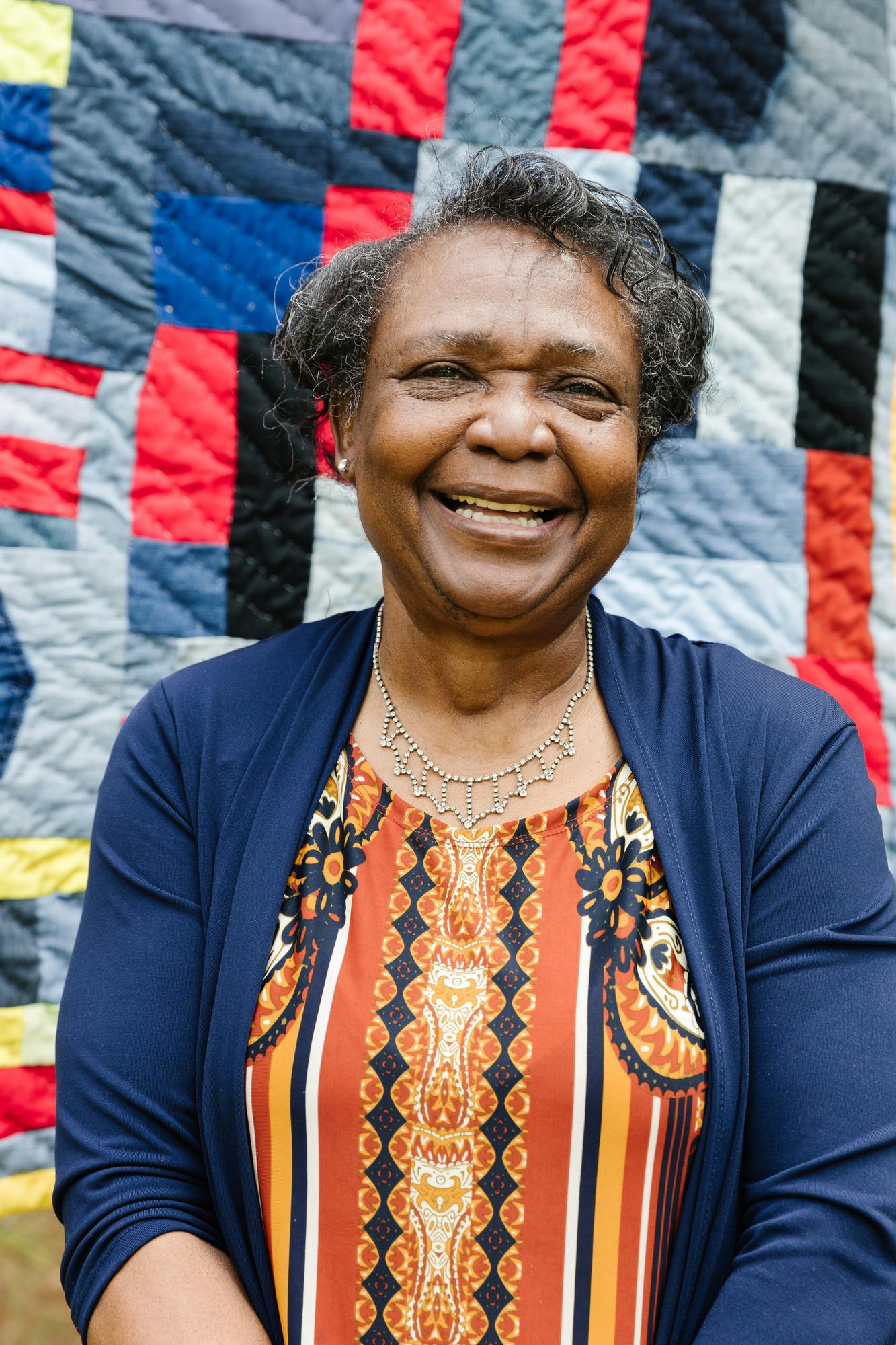 Portrait of textile artist stella mae pettway smiling in front of blue and red quilt