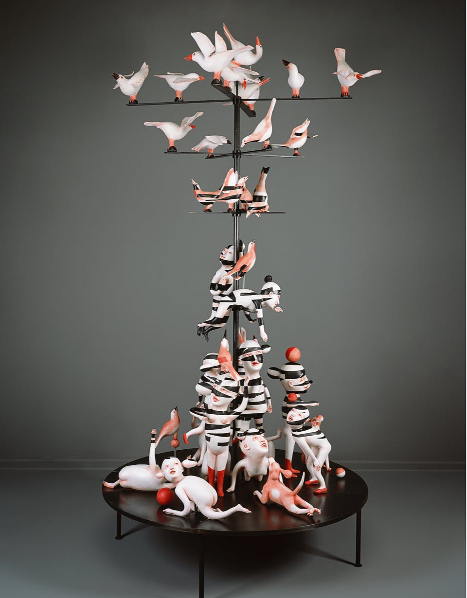black white and pink ceramic sculpture with people dogs and birds arranged on a telephone pole like structure