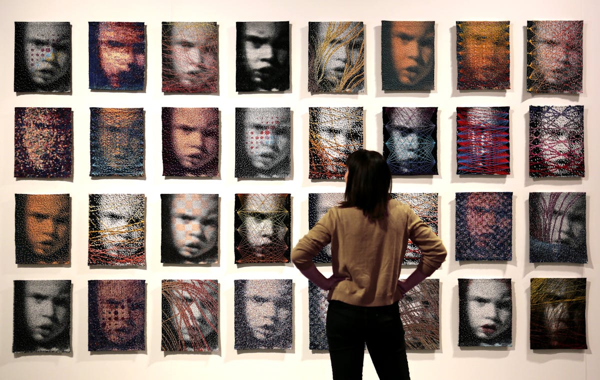 wall installation of an array of the same portrait of a young person made as a textile with different stitching overlaid