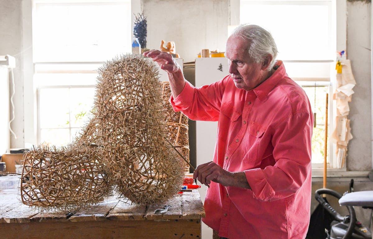 artist in salmon colored shirt wokring in studio on sculpture made from spikey woven twigs
