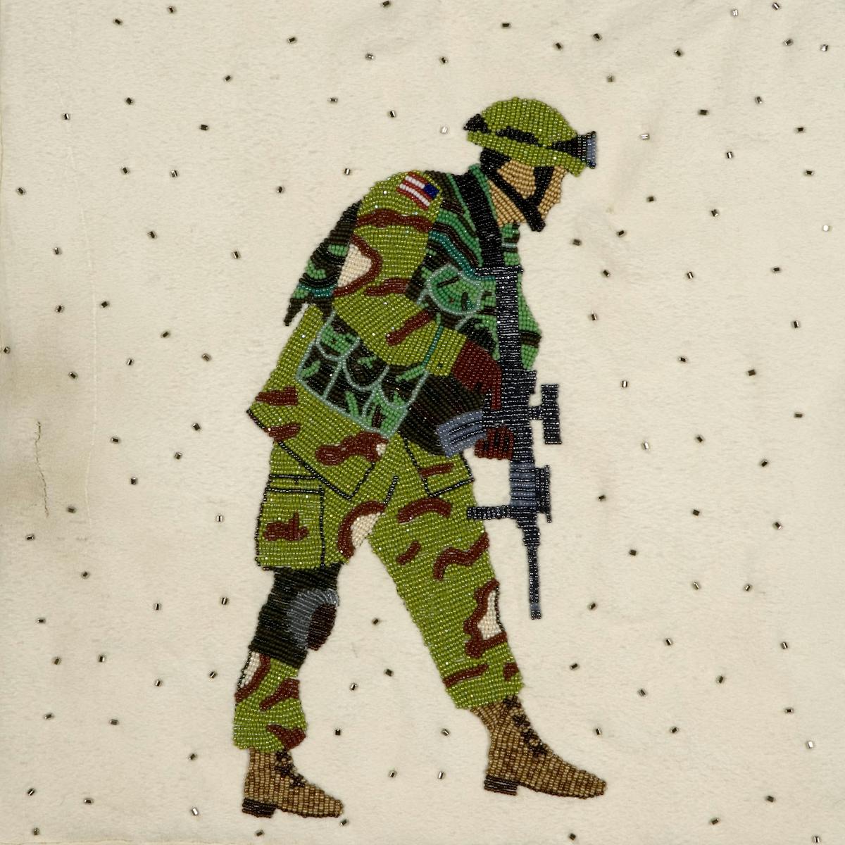 detail of tan blanket with bead embroidered image of a soldier in camoflage carrying an assault rifle