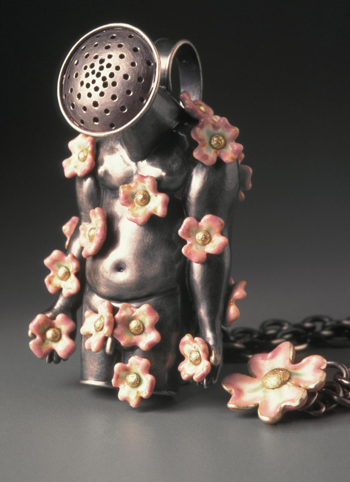 art jewelry necklace with pendant in the shape of a torso with watering can spout for head and covered in pink flowers
