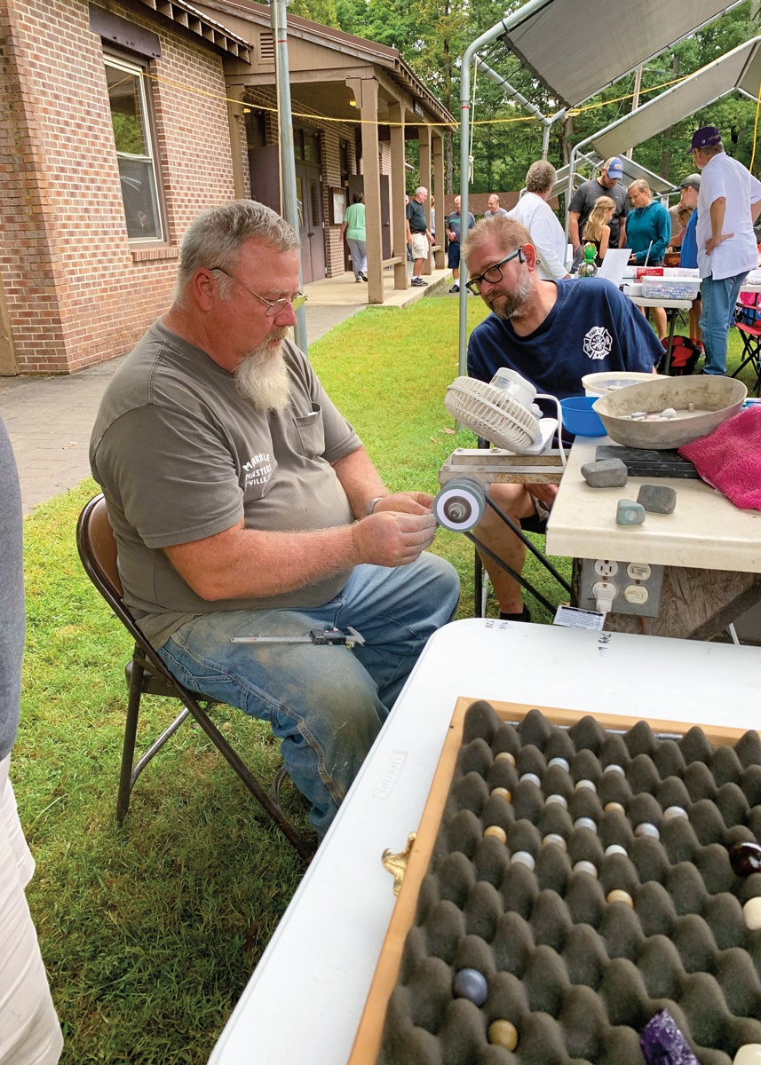 man uses machinery to shape marble at event while another man watches