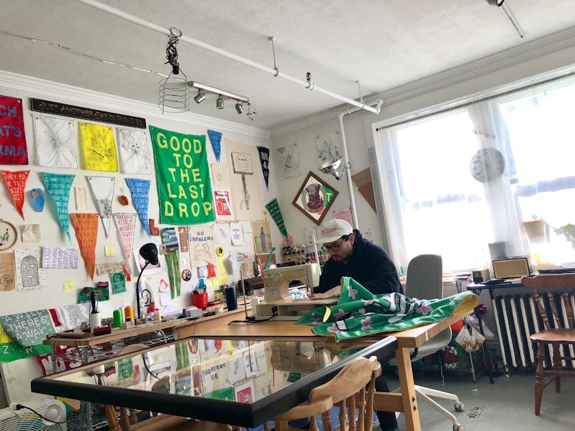 Andy Li working on a sewing machine in a studio with colorful lettered banners on the walls