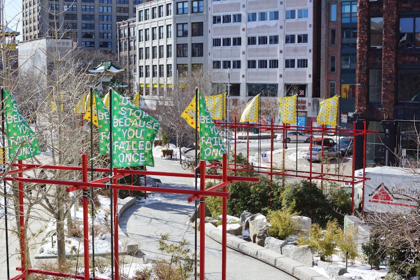 Installation of green and yellow lettered banners on red posts over an outdoor walkway